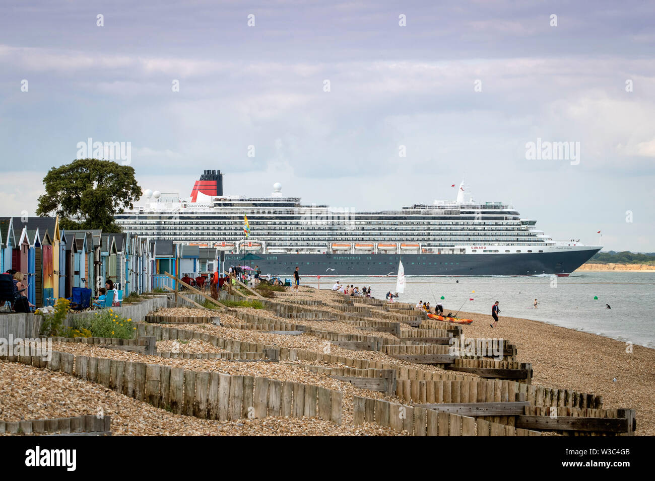 Southampton, Hampshire, Großbritannien. 14. Juli 2019. UK Wetter: Beachgoers genießen ist ein heißer Sommer Abend in Calshot Strand in Southampton als Kreuzfahrtschiff Queen Victoria vorbei. Credit: Stuart Martin/Alamy leben Nachrichten Stockfoto
