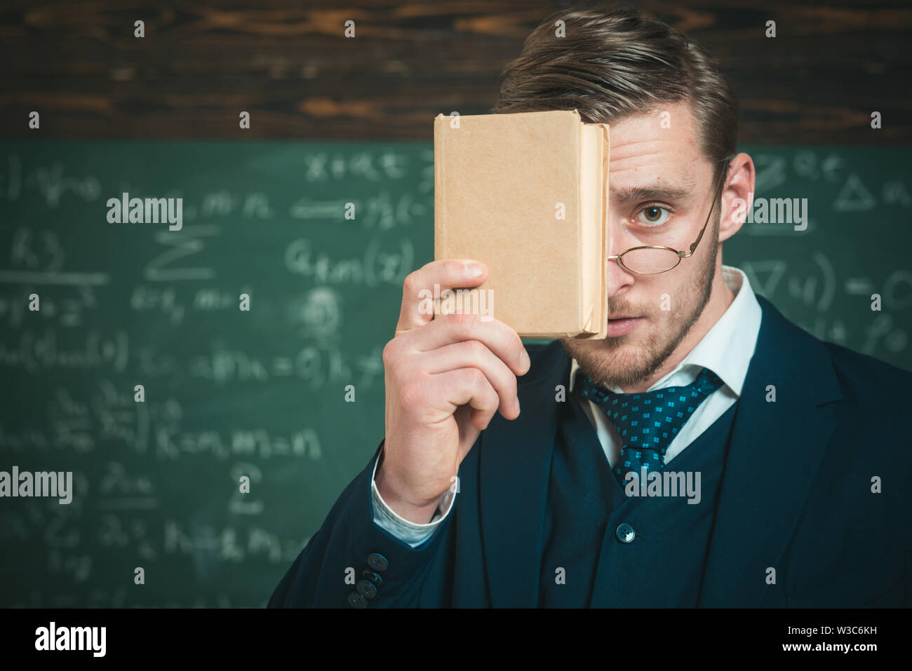 Sie sollten daran denken. Lehrer formale Abnutzung und Gläser sieht Smart, schwarzes Brett Hintergrund. Mann unrasiert hält Buch vor. Lehrer besteht auf Stockfoto