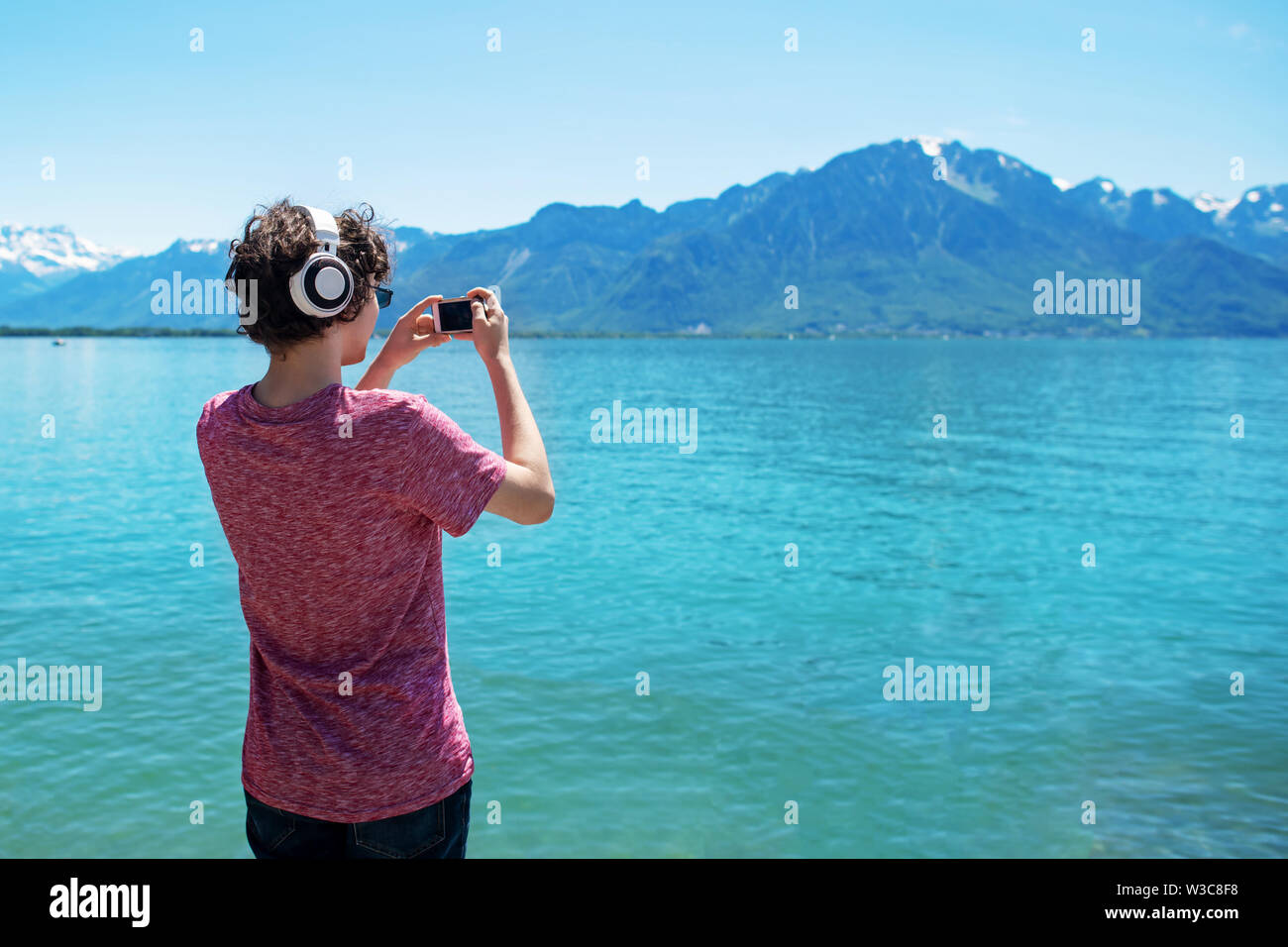 Tennager in Rosa t-shirt und Kopfhörer, Foto, tolle Aussicht auf Alpen auf dem Smartphone am Genfer See. Stockfoto