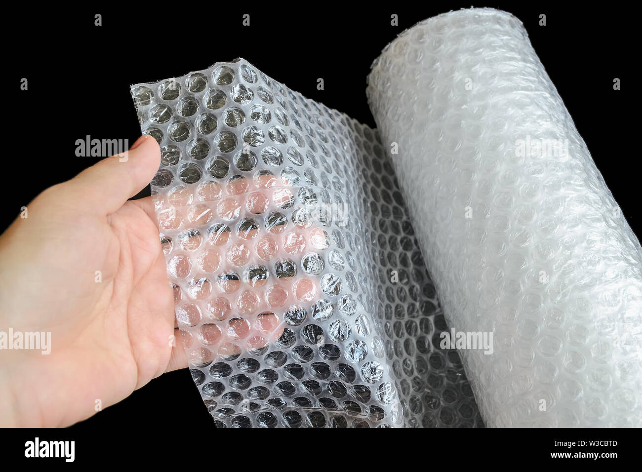 Frau Hand holdind ein weißes Transparent Luftpolsterfolie auf schwarzem Hintergrund. Material für die Verpackung von zerbrechlichen Gegenständen für sicheren Transport. Ansicht von oben. Stockfoto