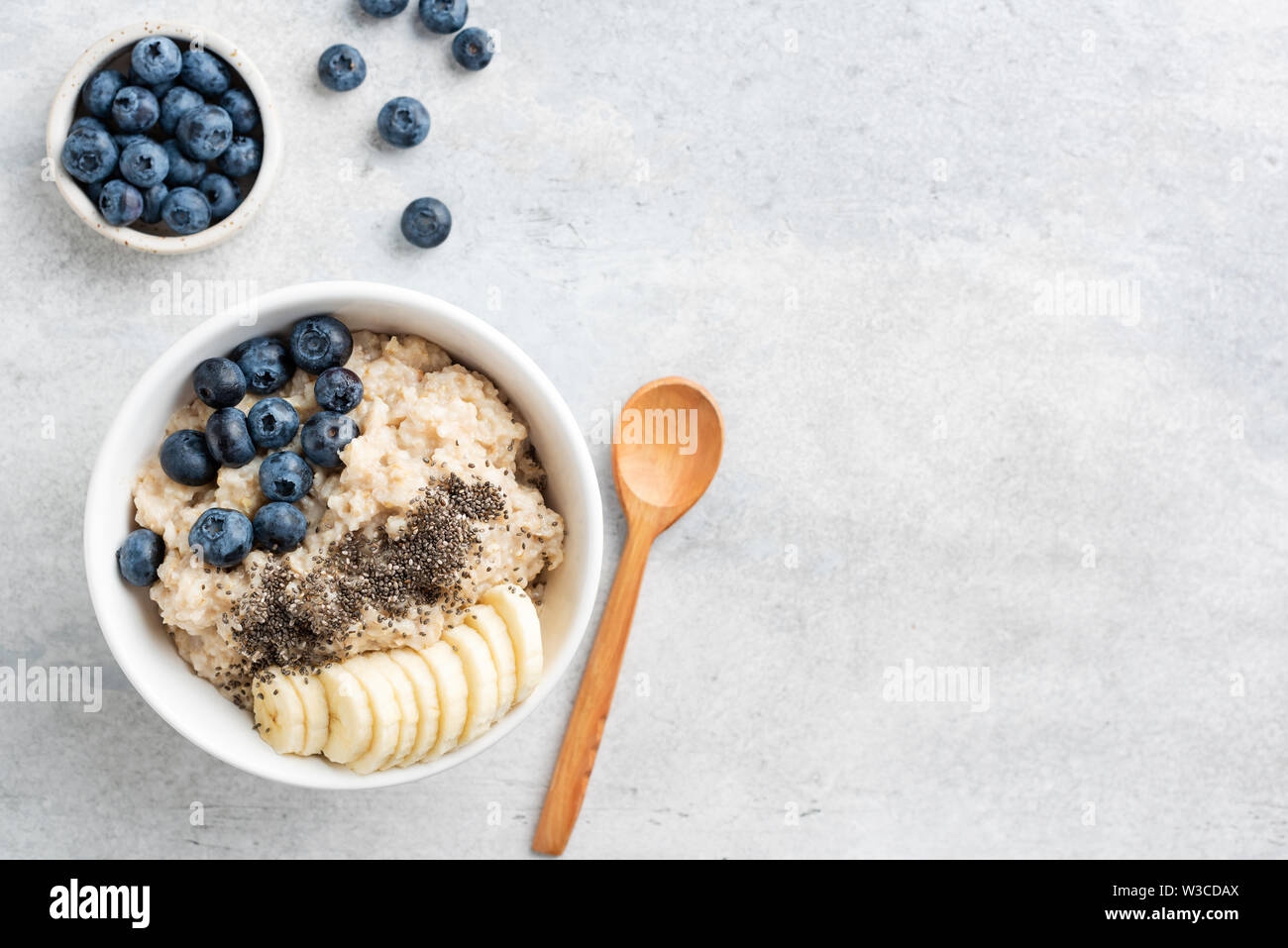 Gesundes Frühstück Haferflocken Schüssel mit Banane, Blaubeere und Chia Samen in Schüssel auf grauem Beton Hintergrund. Ansicht von oben Kopieren Raum Stockfoto