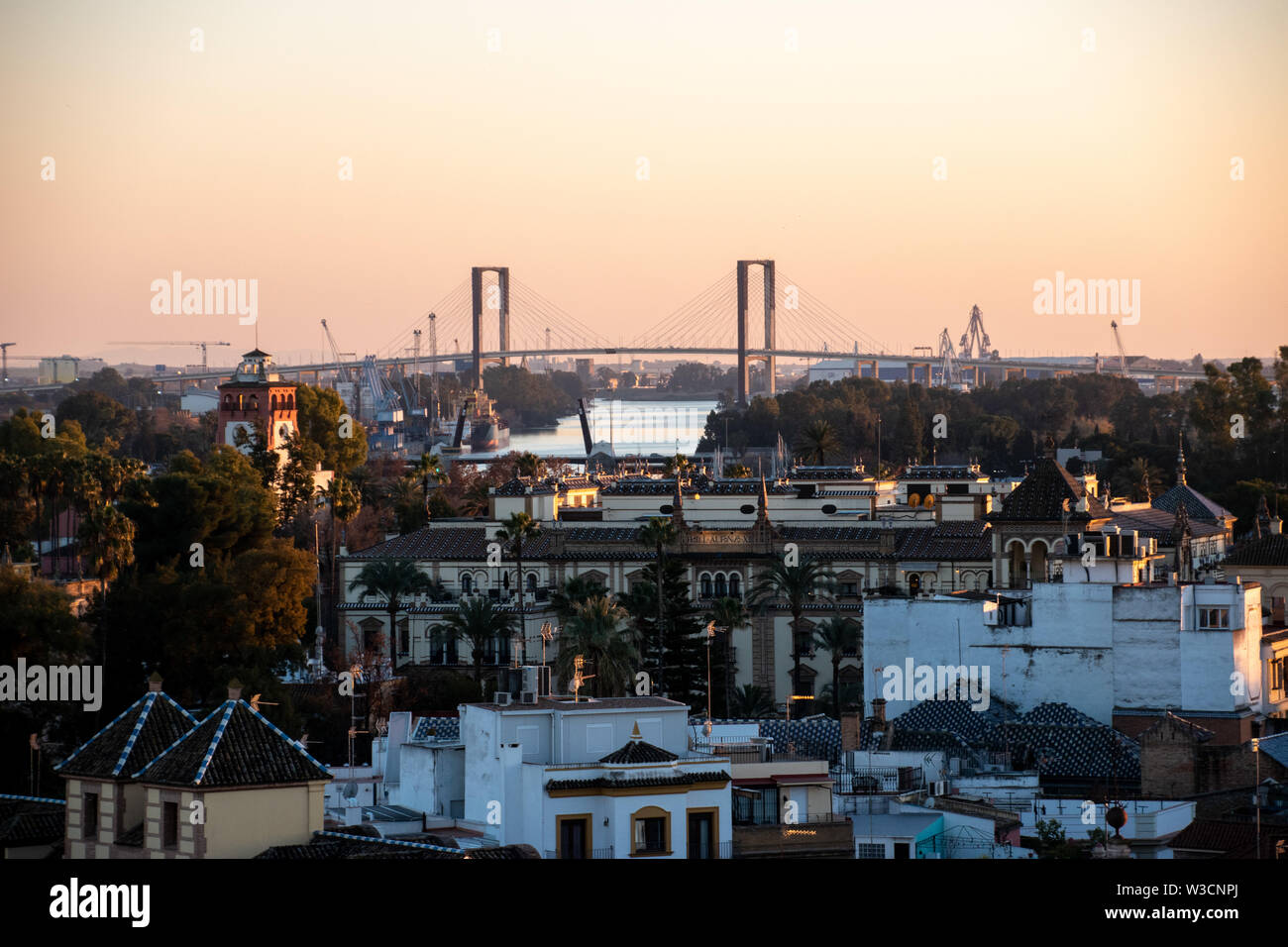 Ein Blick auf die spanische Stadt Sevilla während einer orange Sonnenuntergang mit dem Puente V Centenario über dem Gebäude Stockfoto