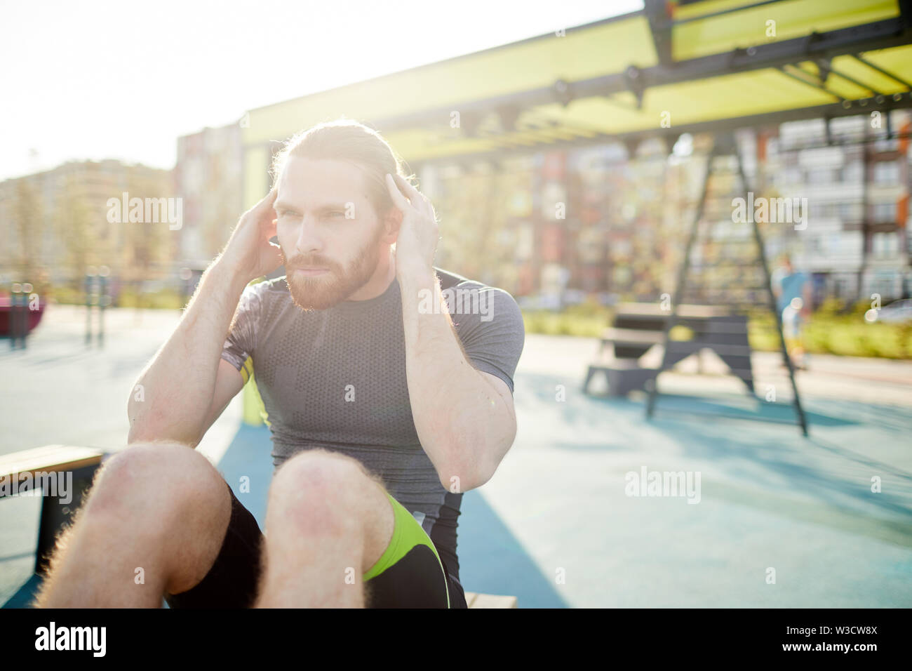 Ernsthafte passen junge bärtige Mann in enger Kleidung tun Knirschen Übung auf öffentlichen Sportplatz, Lichteffekt Stockfoto