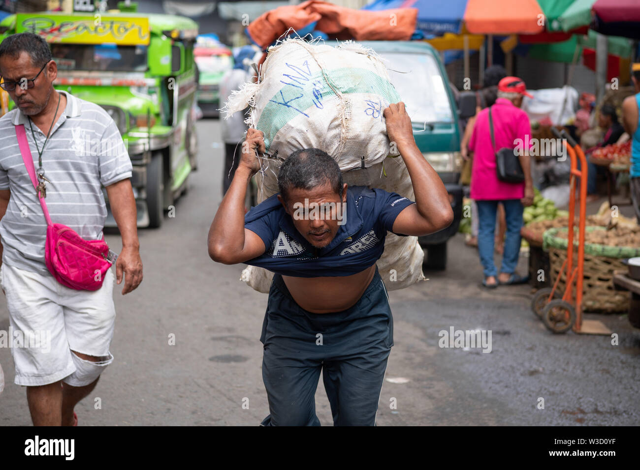 Ein Filipino Mann trägt eine schwere Last von Gemüse auf dem Markt von Cebu City, Philippinen Stockfoto