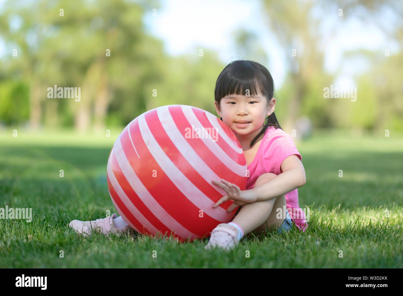 Wenig asiatisches Mädchen posieren mit roten Ball in Park Stockfoto