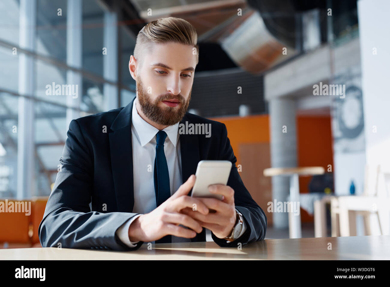 Geschäftsmann mit Bart über sein Smartphone am modernen Arbeitsplatz Stockfoto