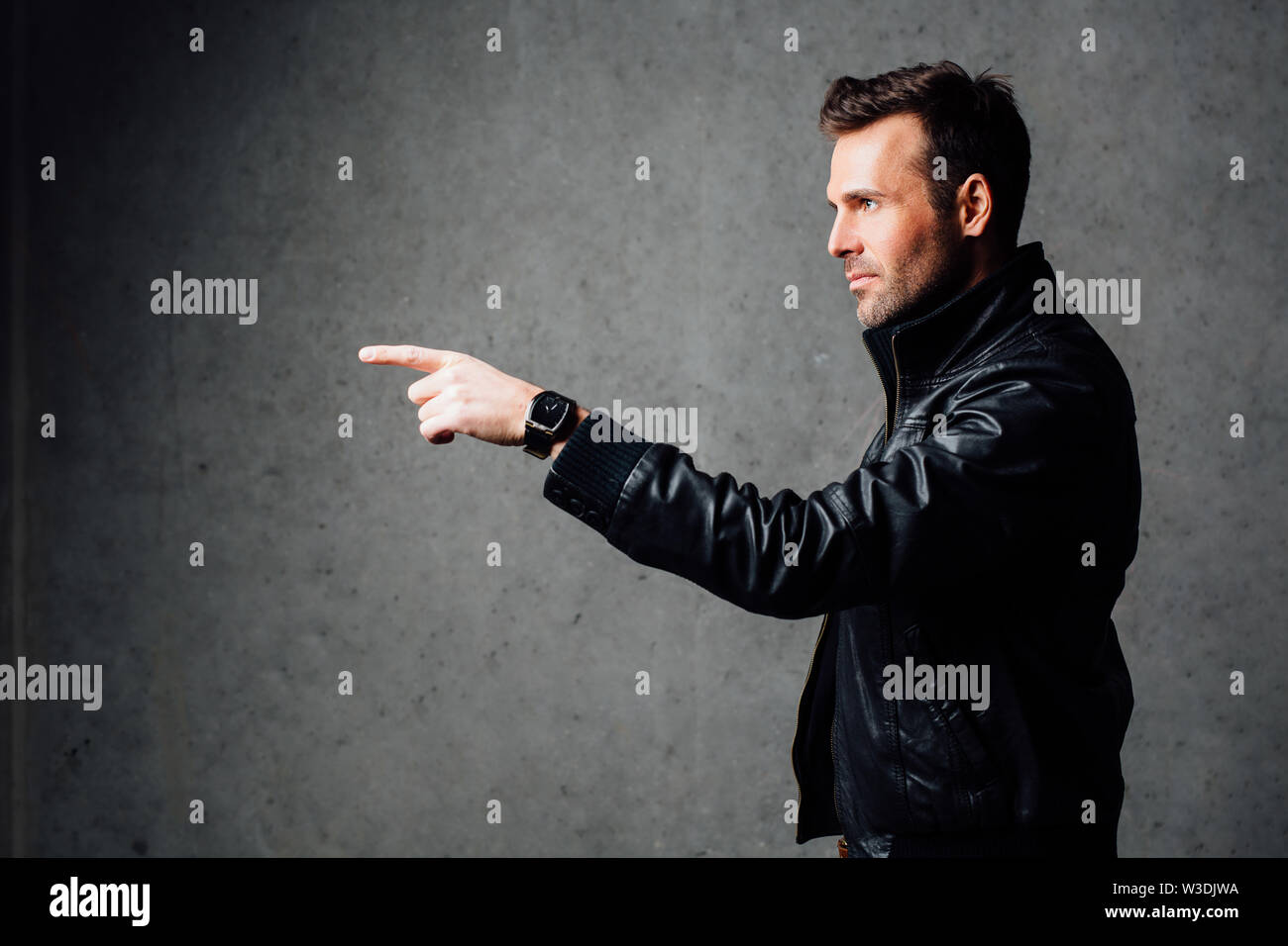 Ernster Mann in Leder Jacke zeigt. Gegen eine Betonwand Stockfoto