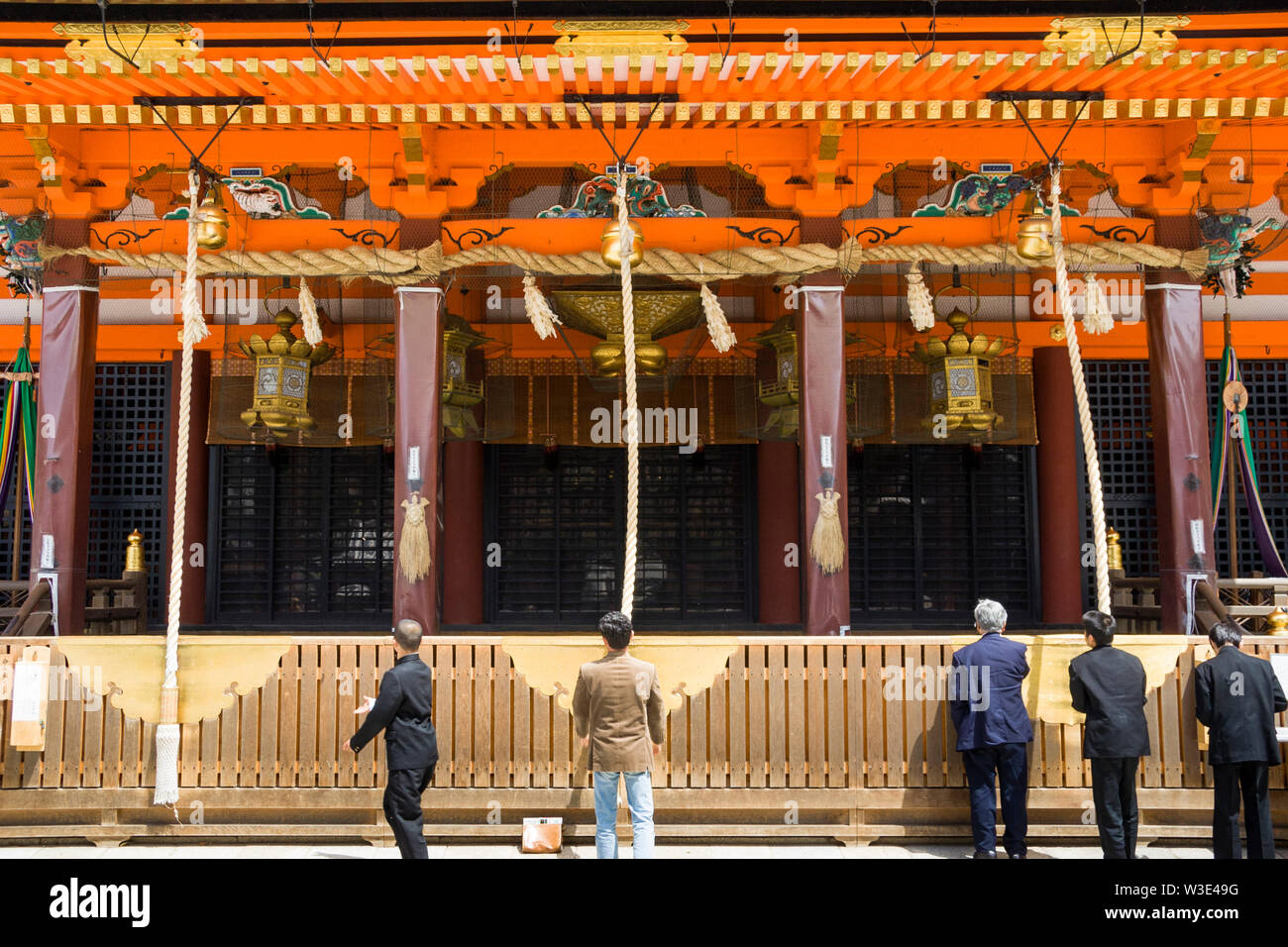 Kyoto, Shinto Yasaka Schrein. Main Hall close up in hellem Sonnenlicht mit fünf Männer vor zu beten, von denen zwei Glocken Seile. Stockfoto