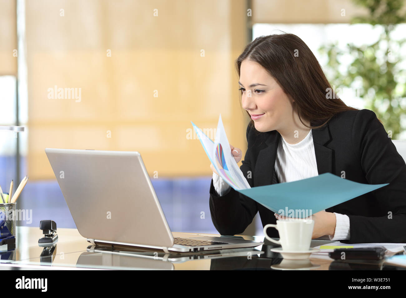 Ernsthafte executive Vergleich Laptop online Inhalte und Dokumente auf Papier im Büro Stockfoto