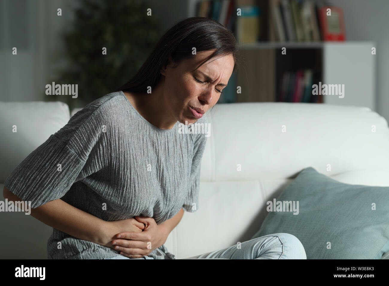 Betonte Frau mit Bauchschmerzen in der Nacht auf einer Couch im Wohnzimmer zu Hause sitzen Stockfoto