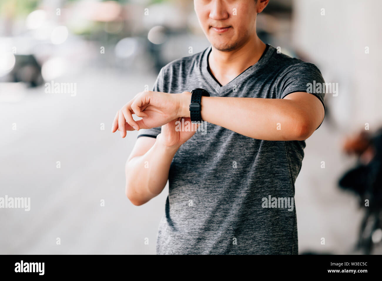 Mann in grauen T-Shirt Prüfung fitness Tracker beim Stehen auf unscharfen Hintergrund der Stadt Straße in Outdoor Training Stockfoto