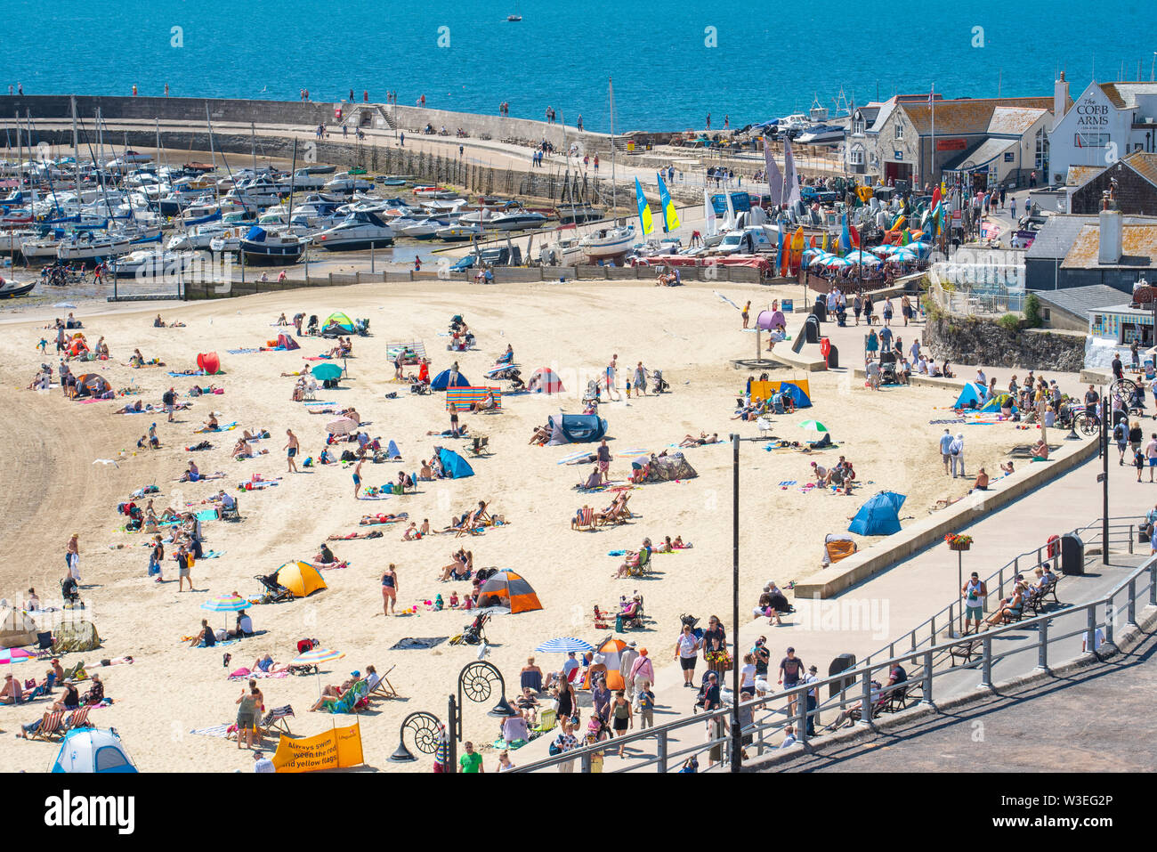 Lyme Regis, Dorset, Großbritannien. 15. Juli 2019. UK Wetter: Sengende Hitze St. Swithin Tag Sonnenschein in Lyme Regis. Besucher entspannen am Strand an der Küste von Lyme Regis an einem heißen und sonnigen St. Swithin's (Swithun's) Tag. Die Legende besagt, dass wenn die Sonne scheint auf St. Swithin's Day dann 40 Tage Sonnenschein werden folgen. Credit: Celia McMahon/Alamy Leben Nachrichten. Stockfoto