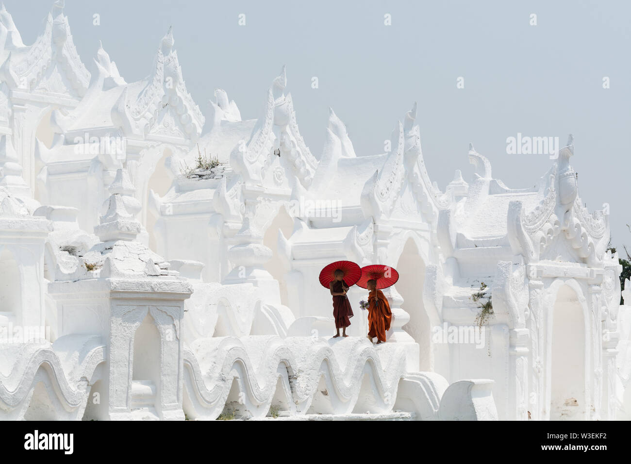 Mandalay, Myanmar - April 2019: Buddhistische Novizen in orangefarbene Gewänder mit roten Sonnenschirme Wandern auf den Wänden der Myatheindan Pagode. Stockfoto