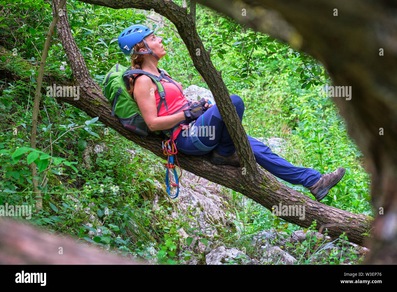 Frau Bergsteiger mit einem blauen Helm ruht auf einem Ast, in Tureni-Copaceni Schlucht, Rumänien. Ihre Kletterausrüstung (tube Belay, prusik Loop, carabine Stockfoto