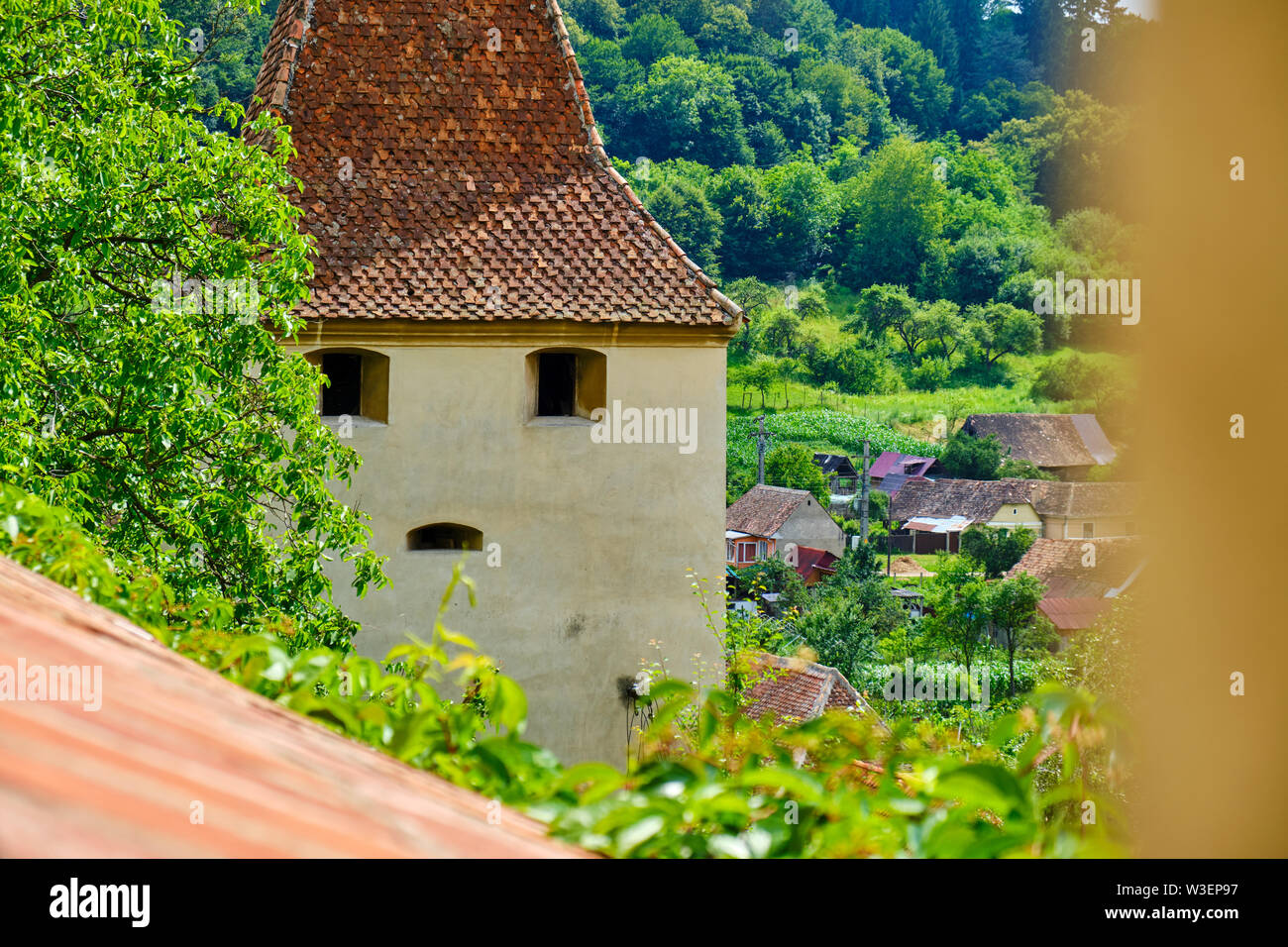 Mittelalterlichen Turm mit Windows wie Augen und Mund, in Birthälm, Rumänien geprägt. Alte Gebäude, das einem menschlichen Gesicht, teilweise hinter einem Baum versteckt. Herkunft Stockfoto