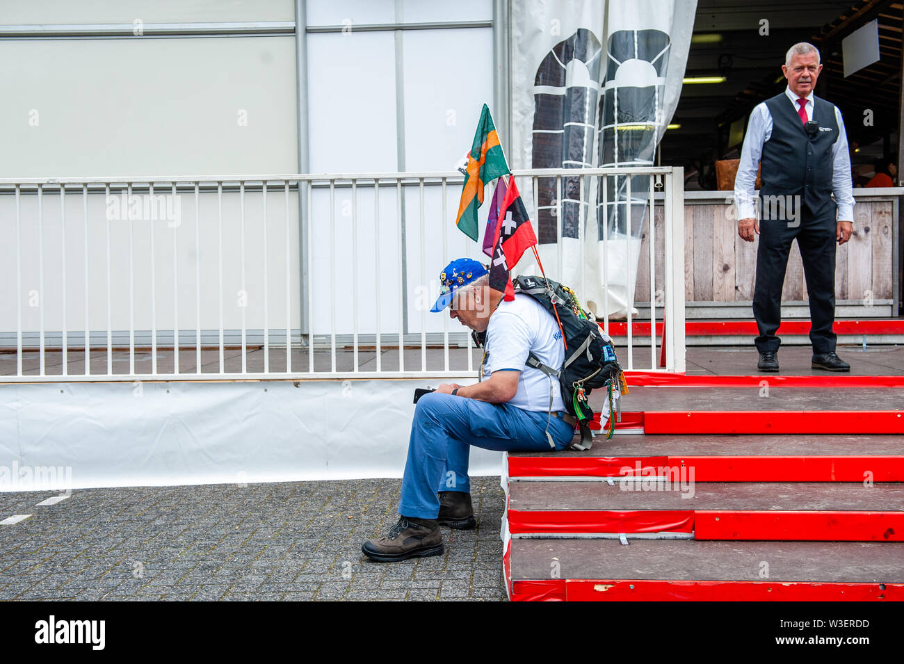 Ein Wanderer sitzt auf der Treppe in der Nähe von einem Security Mann. Die Internationale vier Tage marschiert, genannt "Vierdaagse in Nimwegen in den größten Multi gewachsen ist - Tag Walking Event in der Welt. Der Tag vor, alle Wanderer gehen Ihre Armband mit der Anzahl der Registrierung am Anfang der Spaziergang abzuholen. Stockfoto