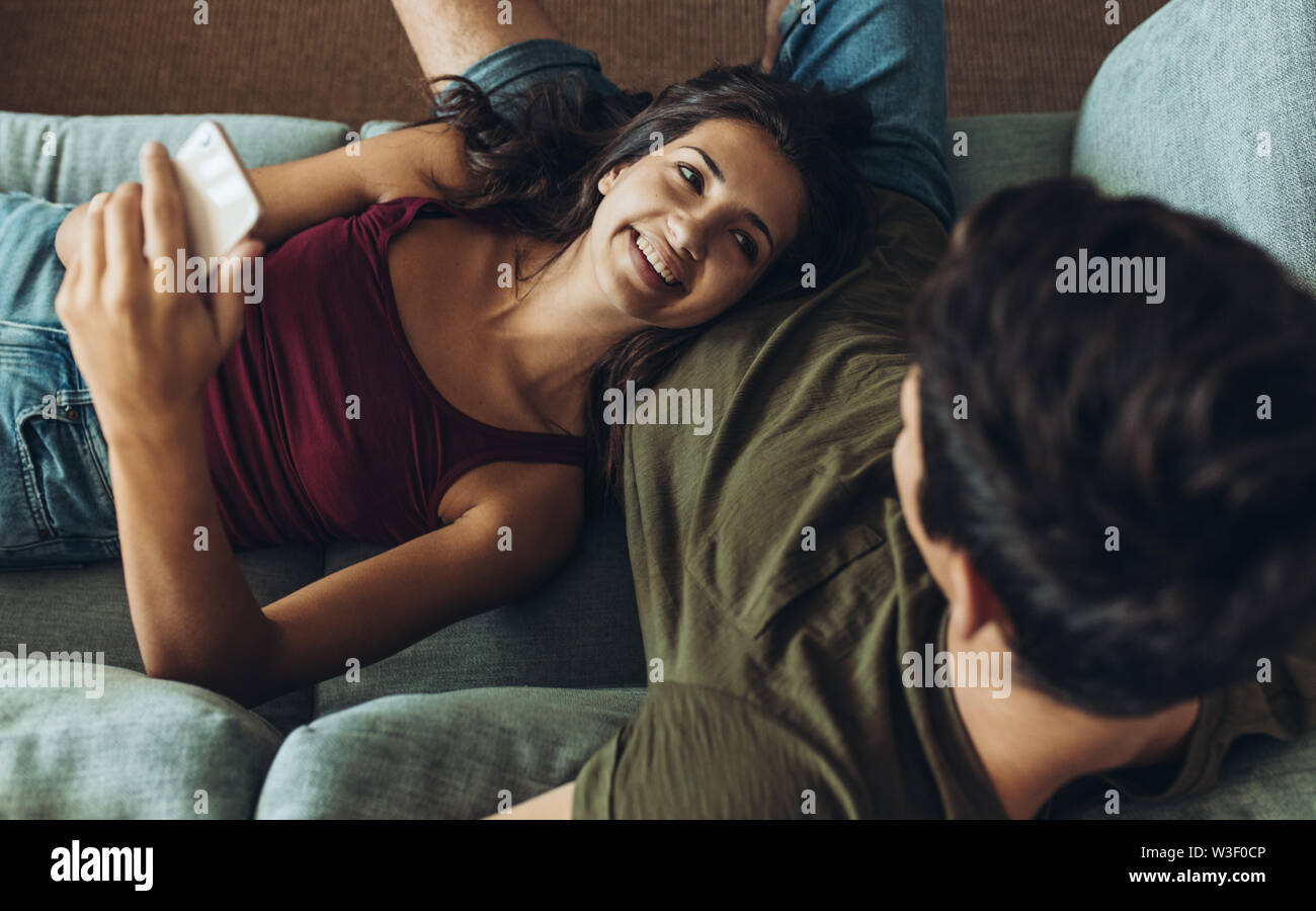 Junge Frau mit smart phone liegen auf Freunde schoß und lächelte. Paar entspannen auf dem Sofa zu Hause. Stockfoto