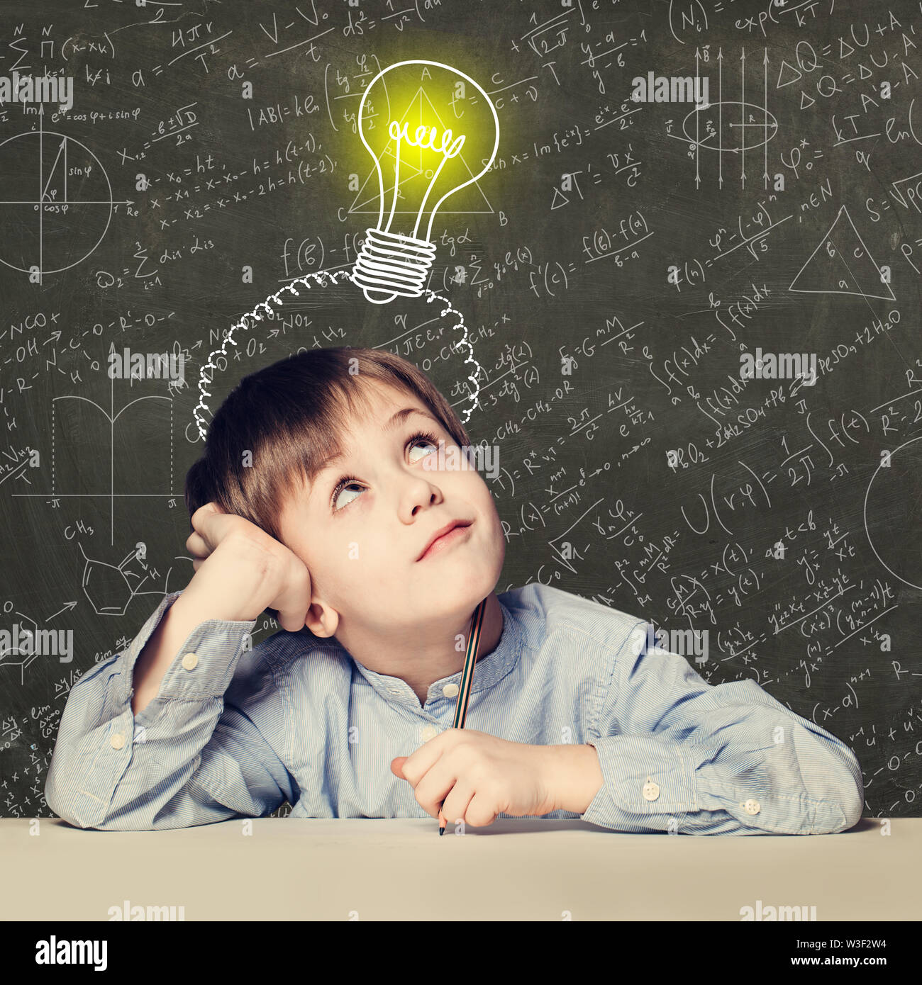 Kind die Schule junge Blick auf Glühbirne auf Hintergrund mit Wissenschaft Formeln Stockfoto