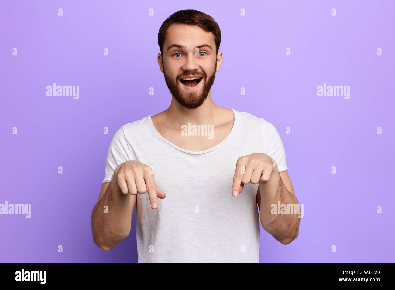 Schöne positive bärtiger Mann nach unten mit zwei Fingern. nach oben Porträt schließen. Isolierte blauen Hintergrund. Studio erschossen. Schauen Sie hier Stockfoto