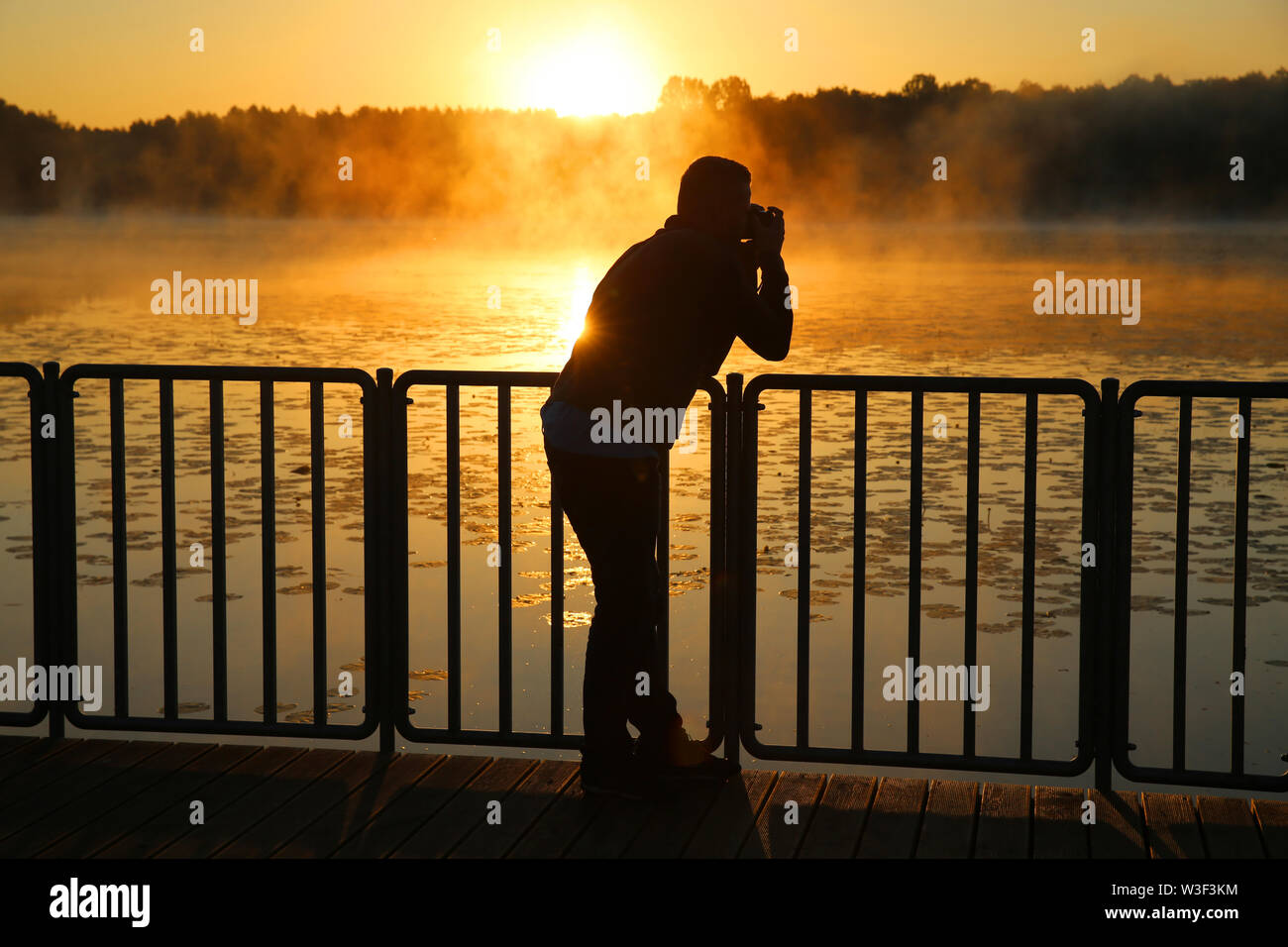 Ein junger Mann fotografieren der Sonnenaufgang über einem See in Polen in den warmen Farben der Sonne Stockfoto