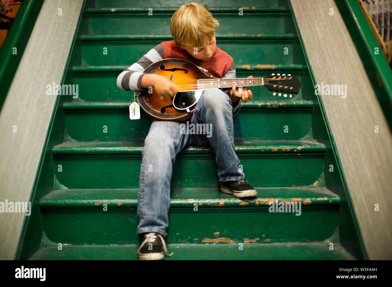 Junge Junge sitzt auf Treppe spielen ein Musikinstrument. Stockfoto