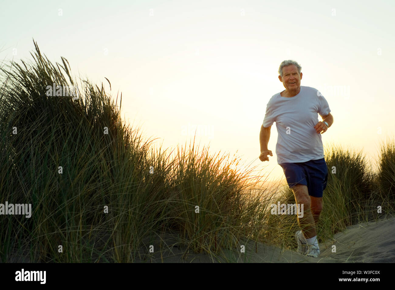 Ältere Menschen joggen auf einer Düne bei Sonnenuntergang. Stockfoto