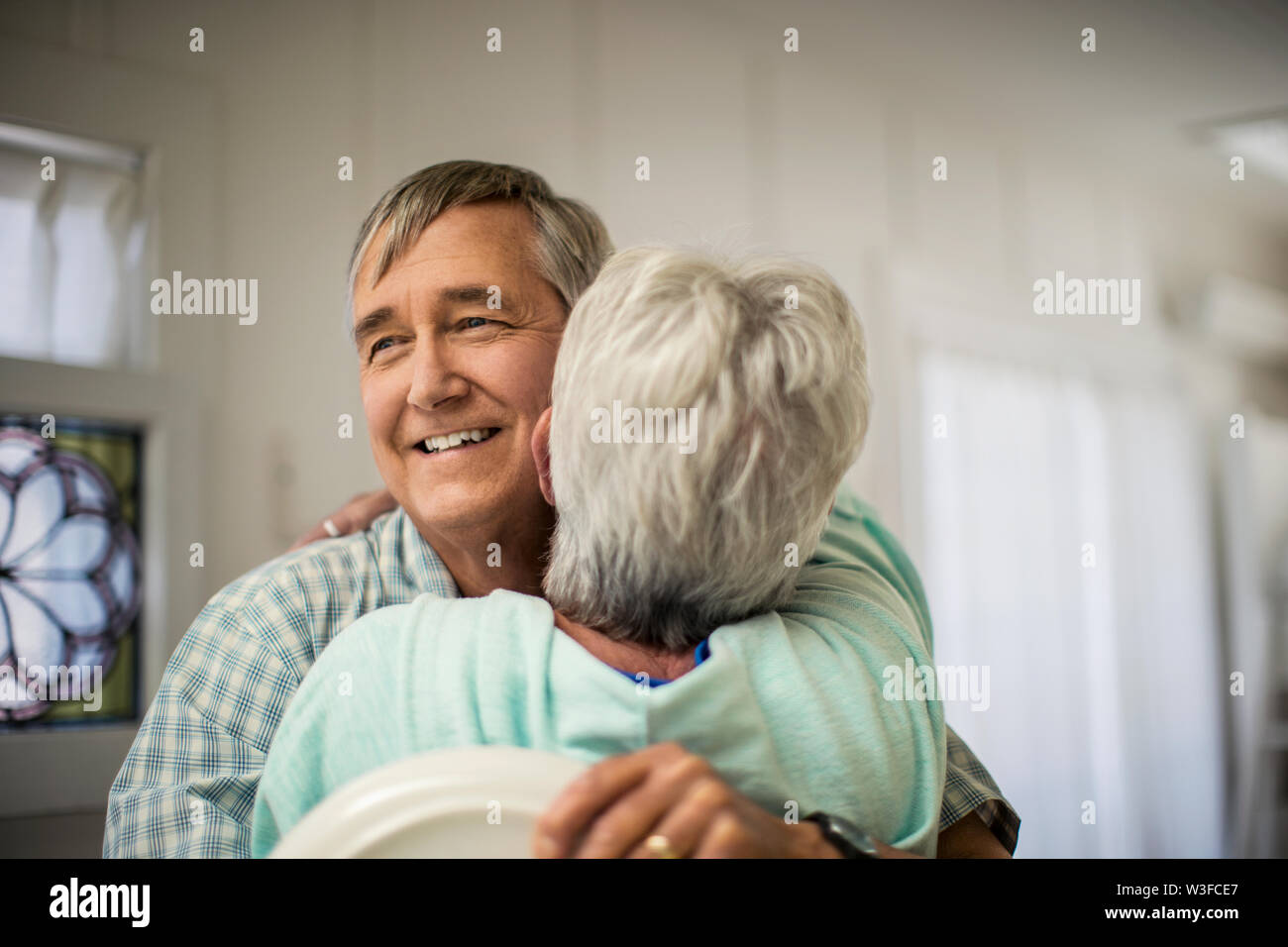 Herzlichen reifes Paar teilen eine spontane Umarmung, wie sie Fertig stellen, um das Geschirr wegräumen. Stockfoto