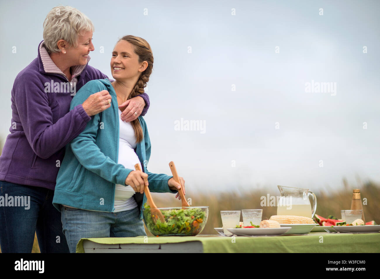 Heiter, reife Frau Umarmungen ihrer schwangeren Tochter, wie sie sich vorbereiten, ein Picknick im Freien. Stockfoto