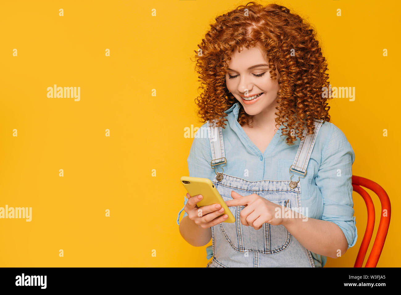 Süße rothaarige Frau in Ihrem Smartphone mit Freunden chatten auf gelbem Hintergrund Stockfoto