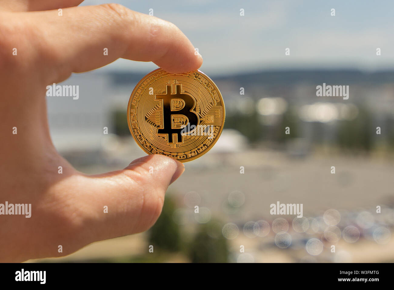 Man Finger halten einen großen runden Golden bitcoin Münze vor der industriellen Stadt. Stockfoto
