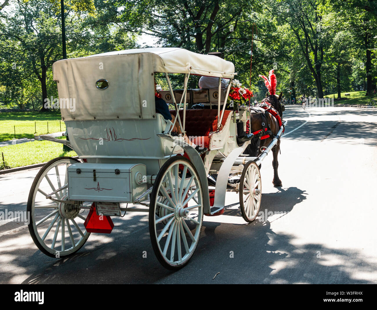 Eine rot-weiße Kutsche ertrinken nimmt Touristen auf einem Rundgang durch den Central Park an einem schönen Sommermorgen. Stockfoto