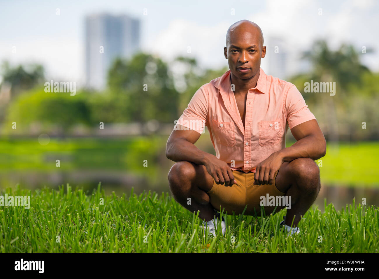 Foto von einem gutaussehenden jungen afrikanischen amerikanischen Mann hocken auf dem Rasen im Park. Deadpan Ausdruck tief in die Kamera starrt Stockfoto