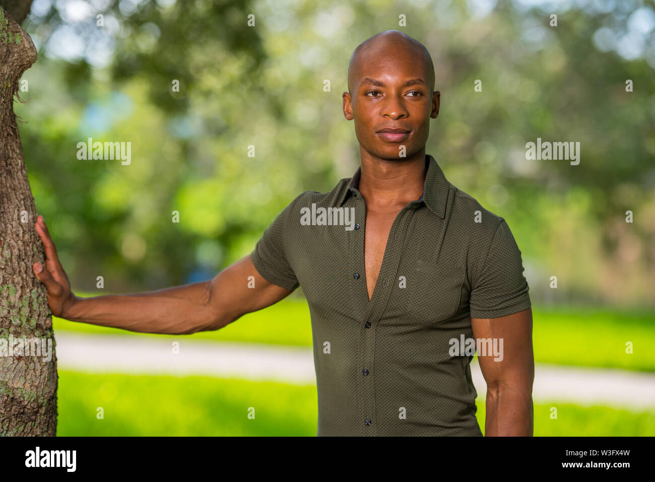 Hübscher junger afrikanischer amerikanischer Mann mit der Hand am Baum im Park posieren. Mans Hemd aufgeknöpft Brust, um zu zeigen wie man weg von der Kamera blicken Stockfoto