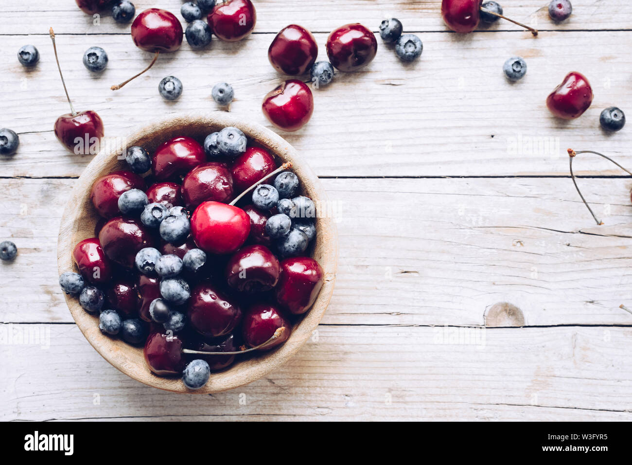 Schüssel von reifen Kirschen und Heidelbeeren. Große Sammlung von frisch gepflückte reife Beeren auf Holz- Hintergrund. Kopieren Sie Platz. Stockfoto