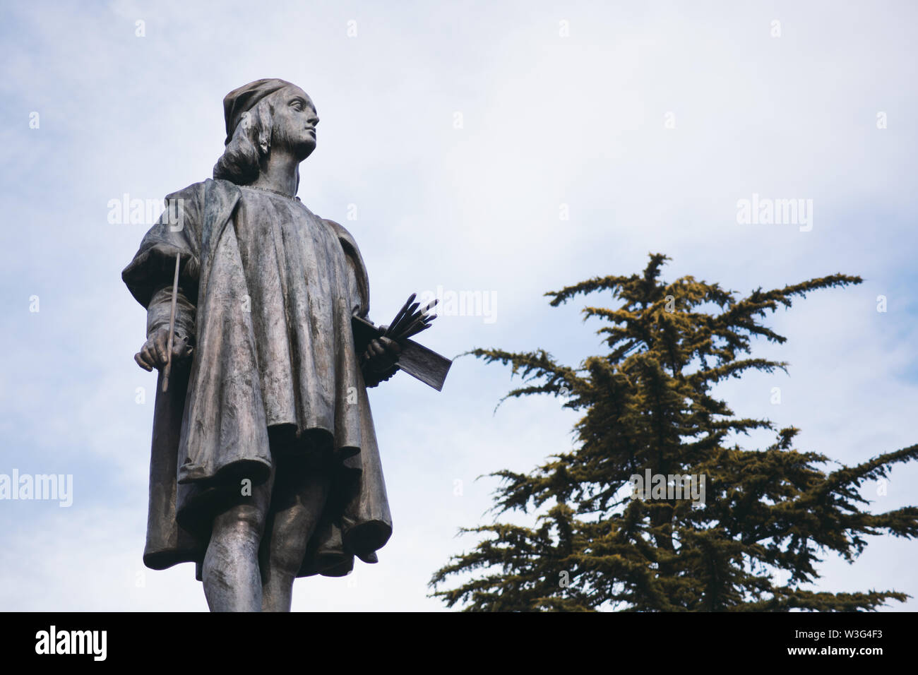 Raffaello Sanzio Statue mit Wolken und Bäumen im Hintergrund - Urbino, Marken, Italien Stockfoto