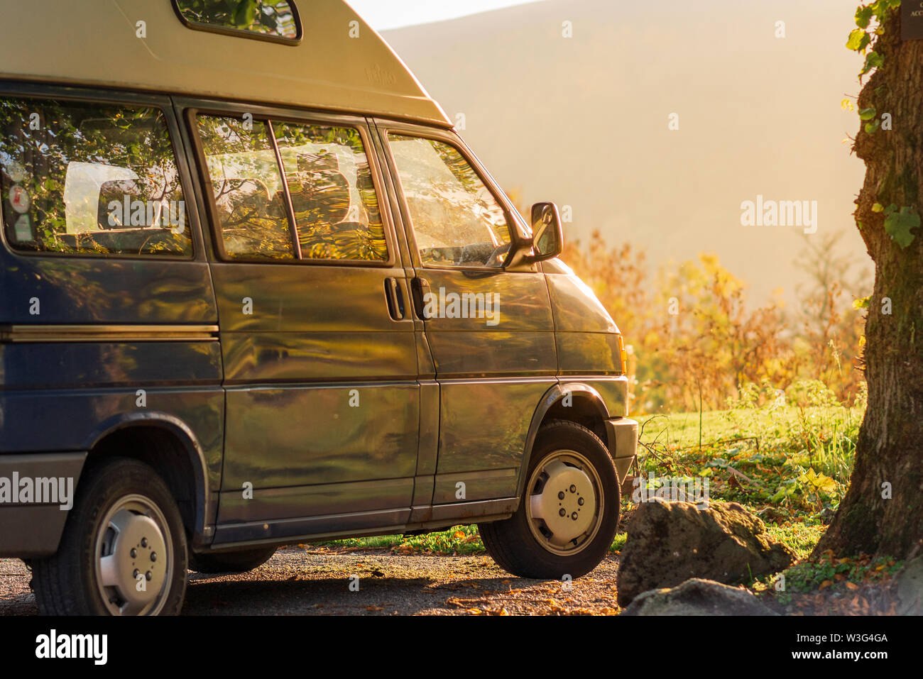 Ein blaues Wohnmobil sitzt bei Sonnenuntergang gegen eine helle grüne Wiese mit üppigen orange Sonnenlicht, das in Stockfoto