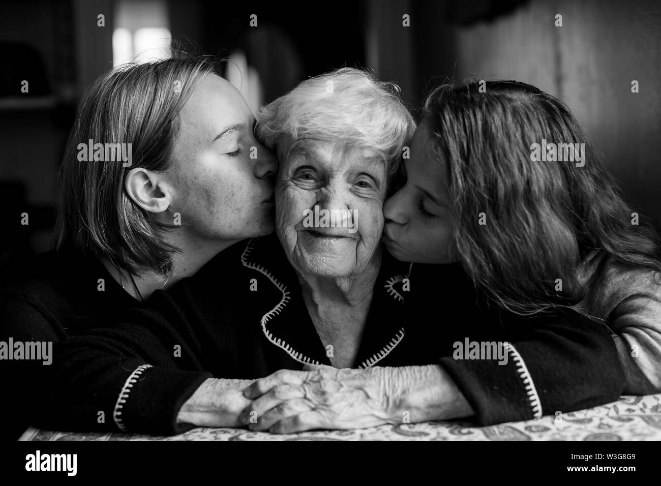 Zwei Mädchen küssen ihre Großmutter. Schwarz-weiß-Porträt. Stockfoto