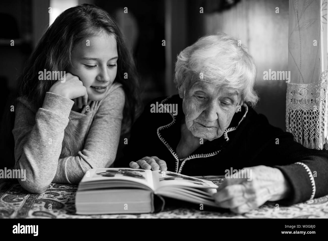 Eine alte Frau - eine Oma mit einem kleinen Mädchen - Enkelin, ein Buch zu lesen. Die Schwarz-Weiß-Fotografie. Stockfoto