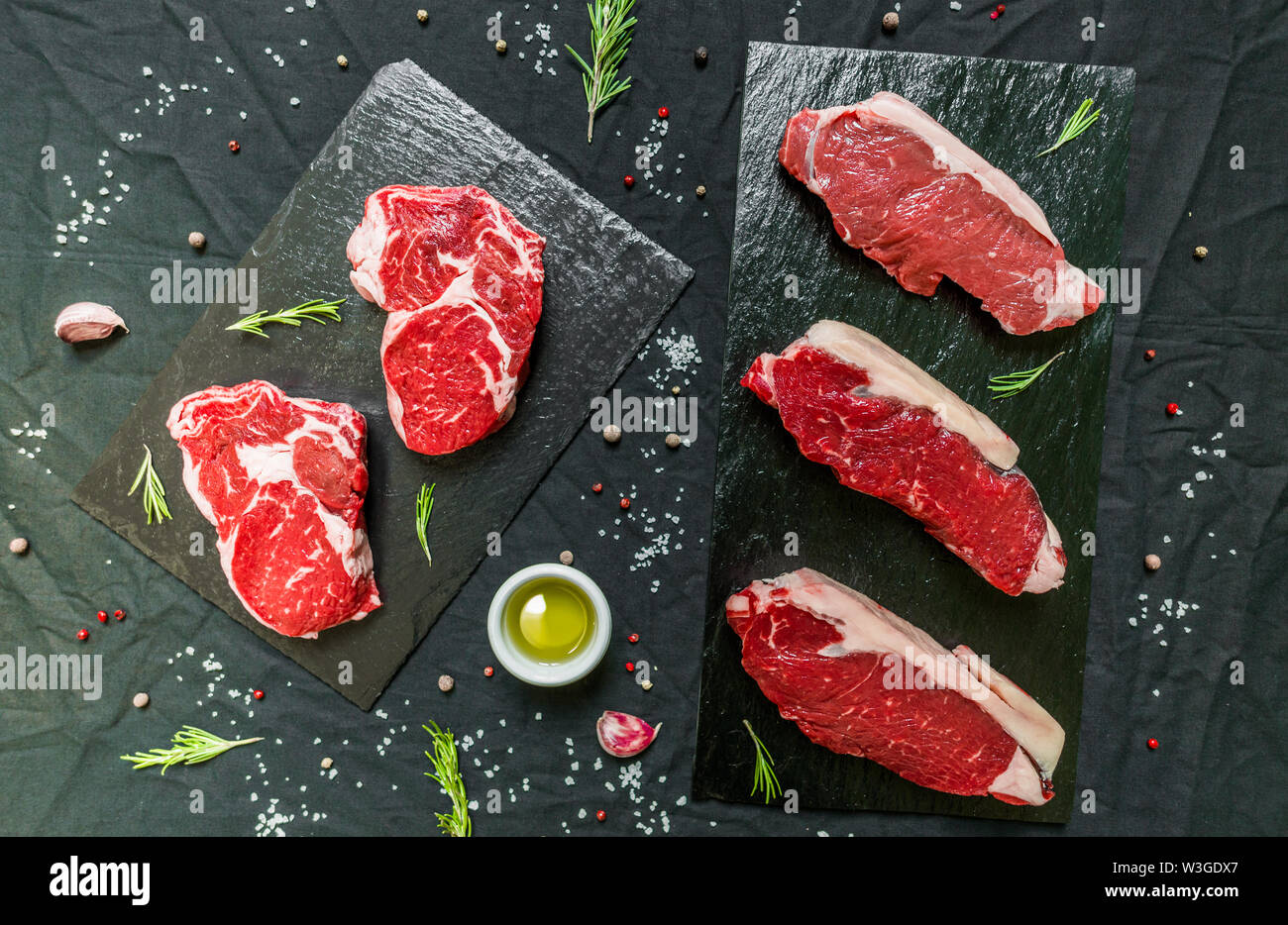 Rindfleisch Rind fleisch Steaks mit Gewürzen und Kräutern auf schwarzem Hintergrund Stockfoto