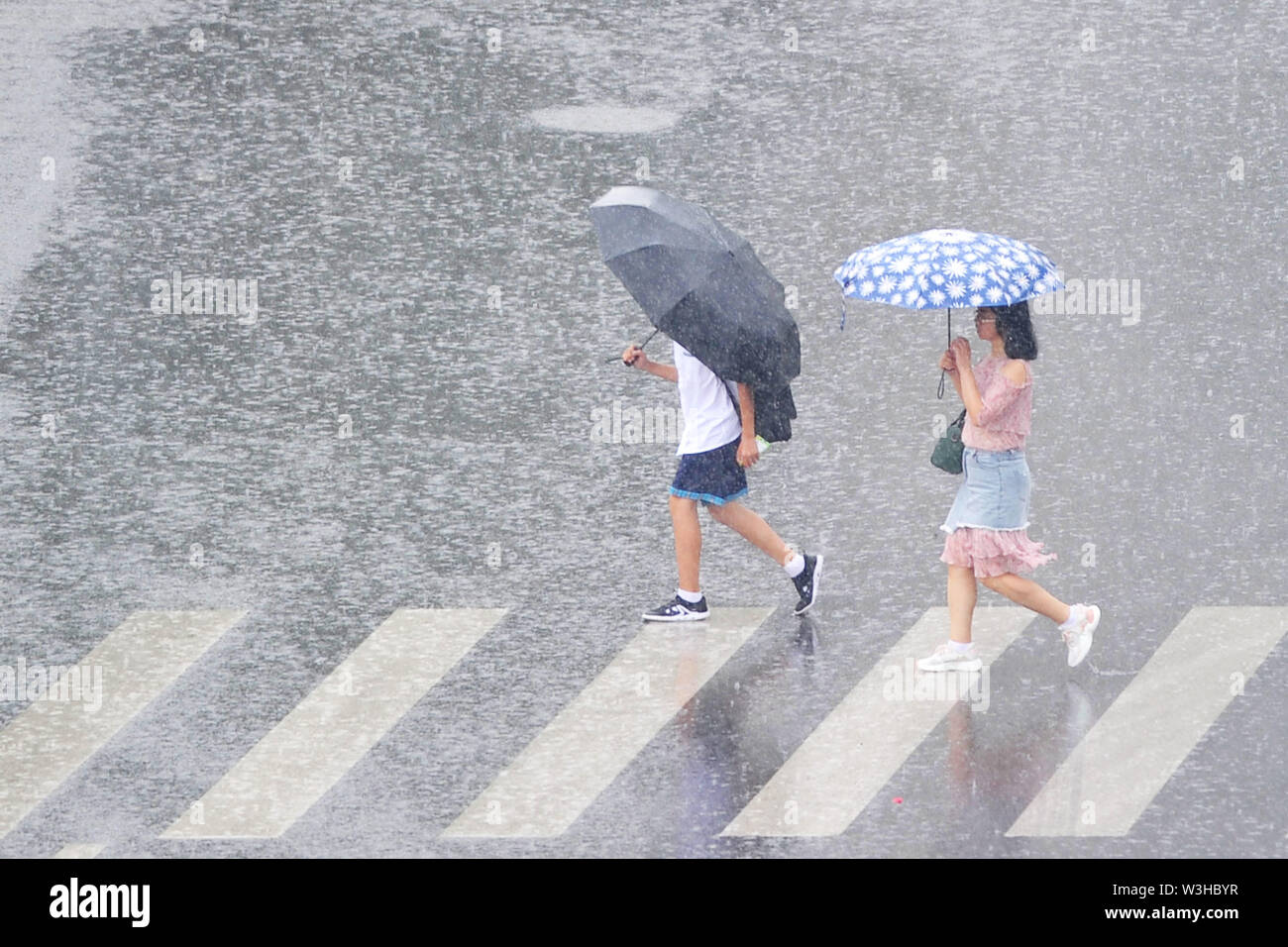 Liaoning, Liaoning, China. 16. Juli, 2019. Liaoning, China - 15. Juli 2019: gehen die Menschen im Regen auf Hua quan Street in Dalian City. Die Liaoning Provincial meteorologische Katastrophe Überwachung und Warnung Center ausgestellt eine blaue Warnsignal für Gewitter Stürme am 13:17 am 15. Juli. Credit: SIPA Asien/ZUMA Draht/Alamy leben Nachrichten Stockfoto