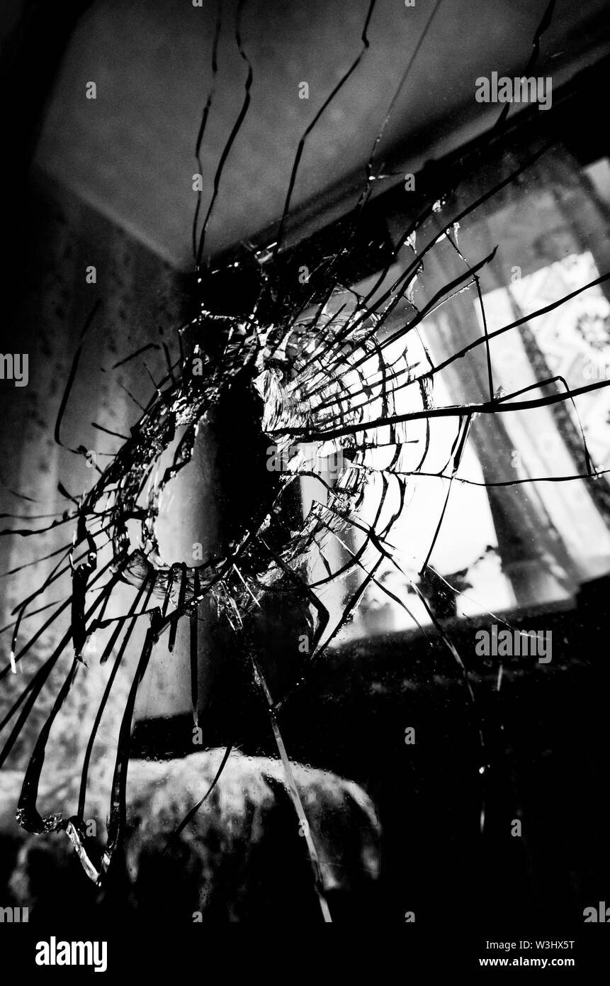 Zerbrochenes Glas mit Rissen und ein Loch stilisierten Schwarzweiß-Film und Lomography im Hintergrund der Fenster im Zimmer Stockfoto