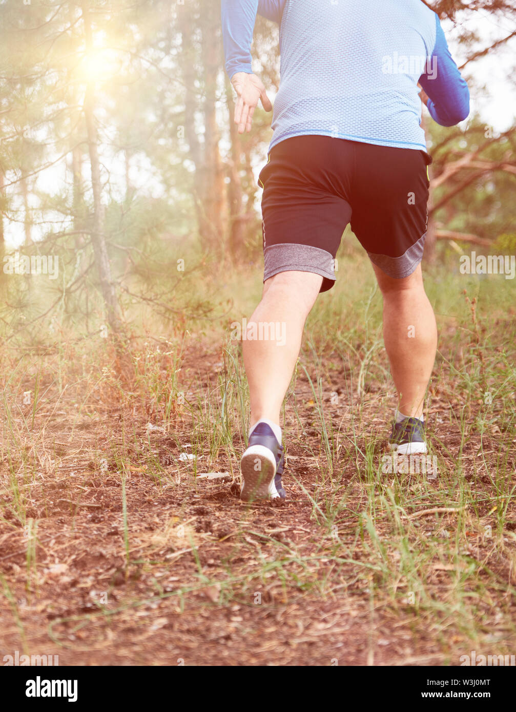 Erwachsenen Mann in Blau Kleidung und schwarze Shorts läuft im Nadelwald gegen die helle Sonne, Konzept für einen gesunden Lebensstil in der Fr Stockfoto