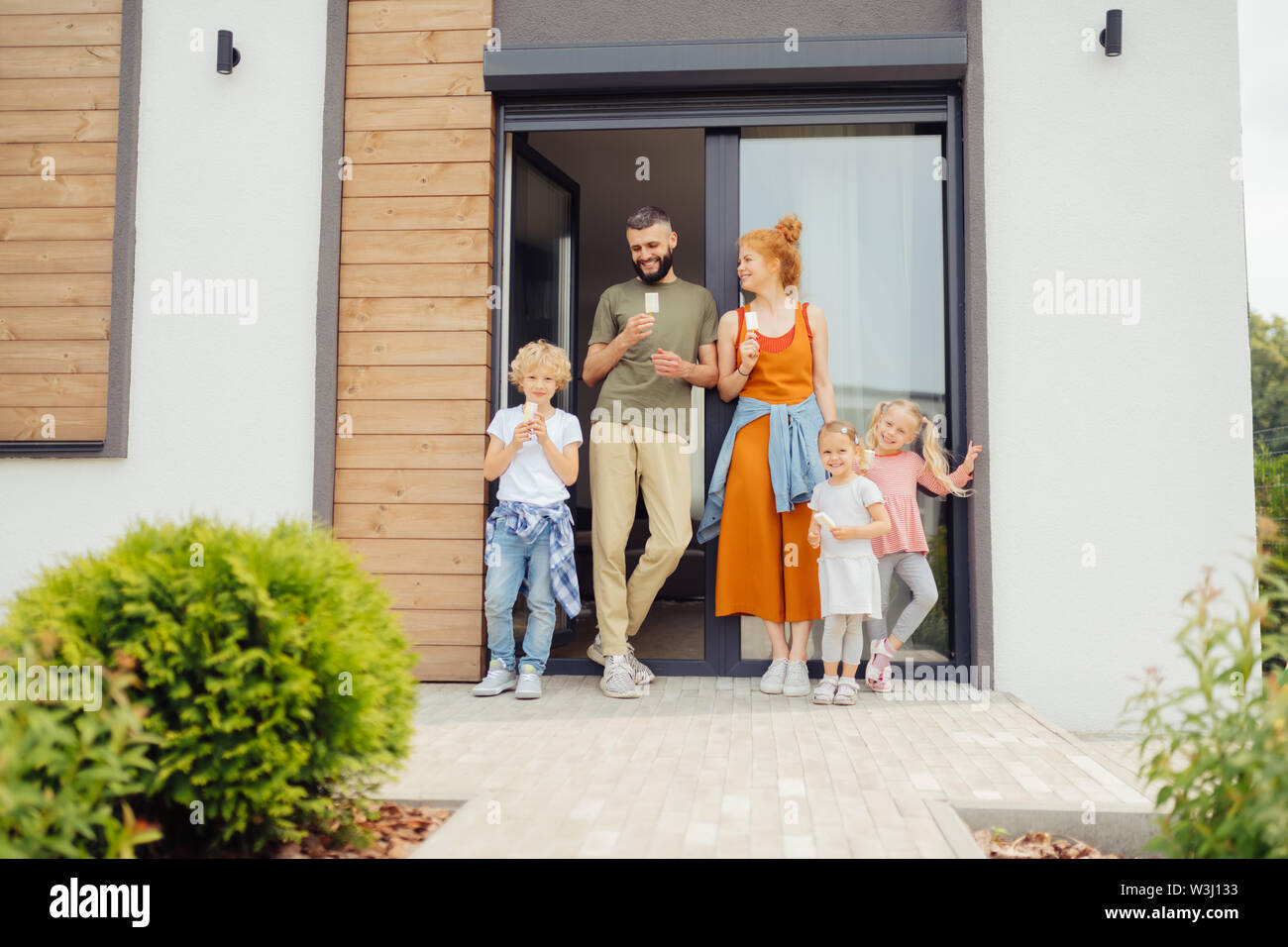Ideal große Familie. Gerne nette Kinder lächeln beim Stehen mit ihren Eltern in der Nähe des Hauses Stockfoto