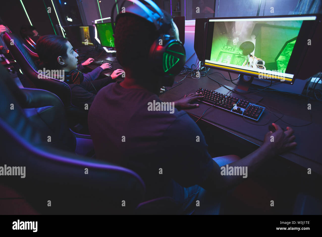 Ansicht der Rückseite des Süchtigen Spieler am Tisch saßen und auf Monitoren beim Spielen online Multiplayer Game Stockfoto