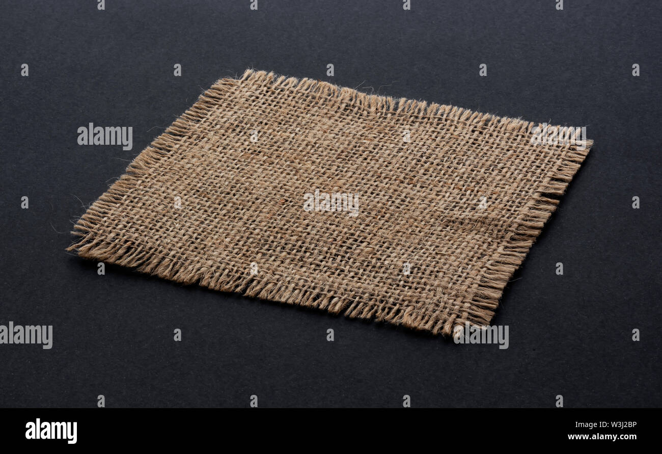Alte sackleinen Stoff serviette Nahaufnahme. Grobes Leinen, Jute sack Stück auf schwarzem Hintergrund isoliert. Hessische Textur Tuch tag mit ausgefransten Rändern. Dark sa Stockfoto