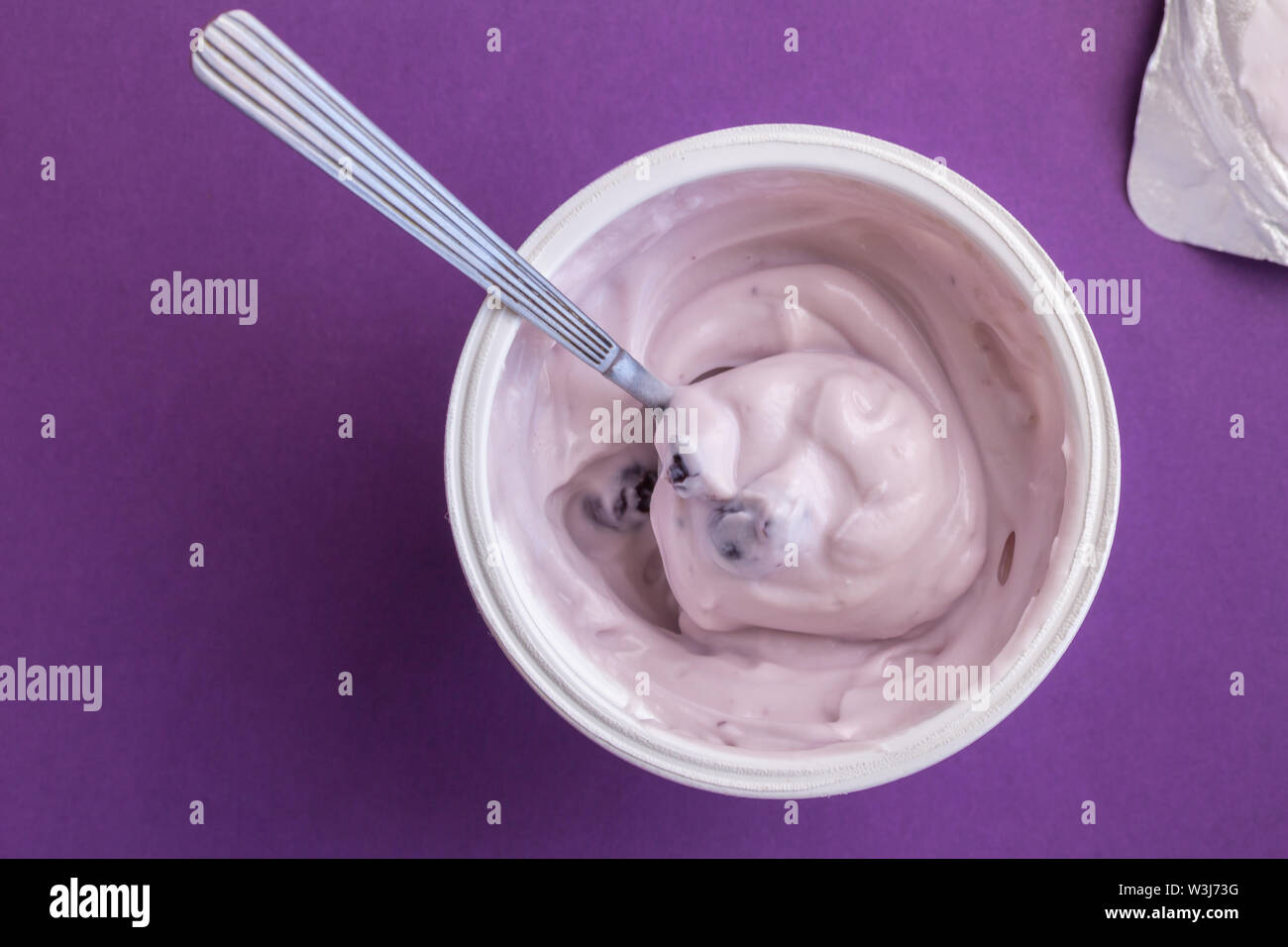 Joghurt becher mit Blue Berry Joghurt, Löffel und Folien Deckel auf lila Hintergrund isoliert - Ansicht von oben Foto Stockfoto