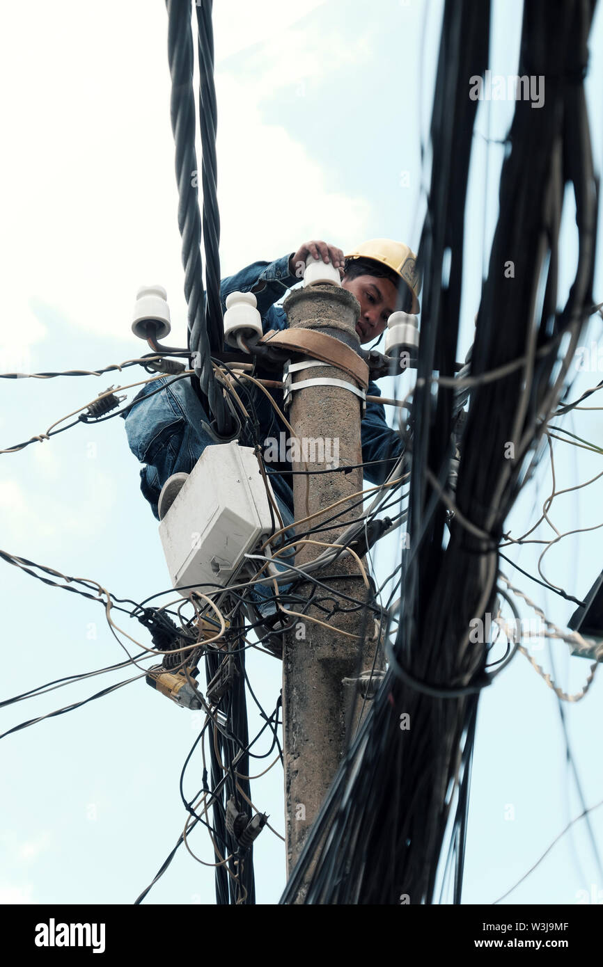 Vietnamesische Strom worker klettern hoch auf elektrische post Strom Netzwerk, Mann Arbeit in unsicheren Service am Mittag, Vietnam, Ho Chi Minh City Stockfoto