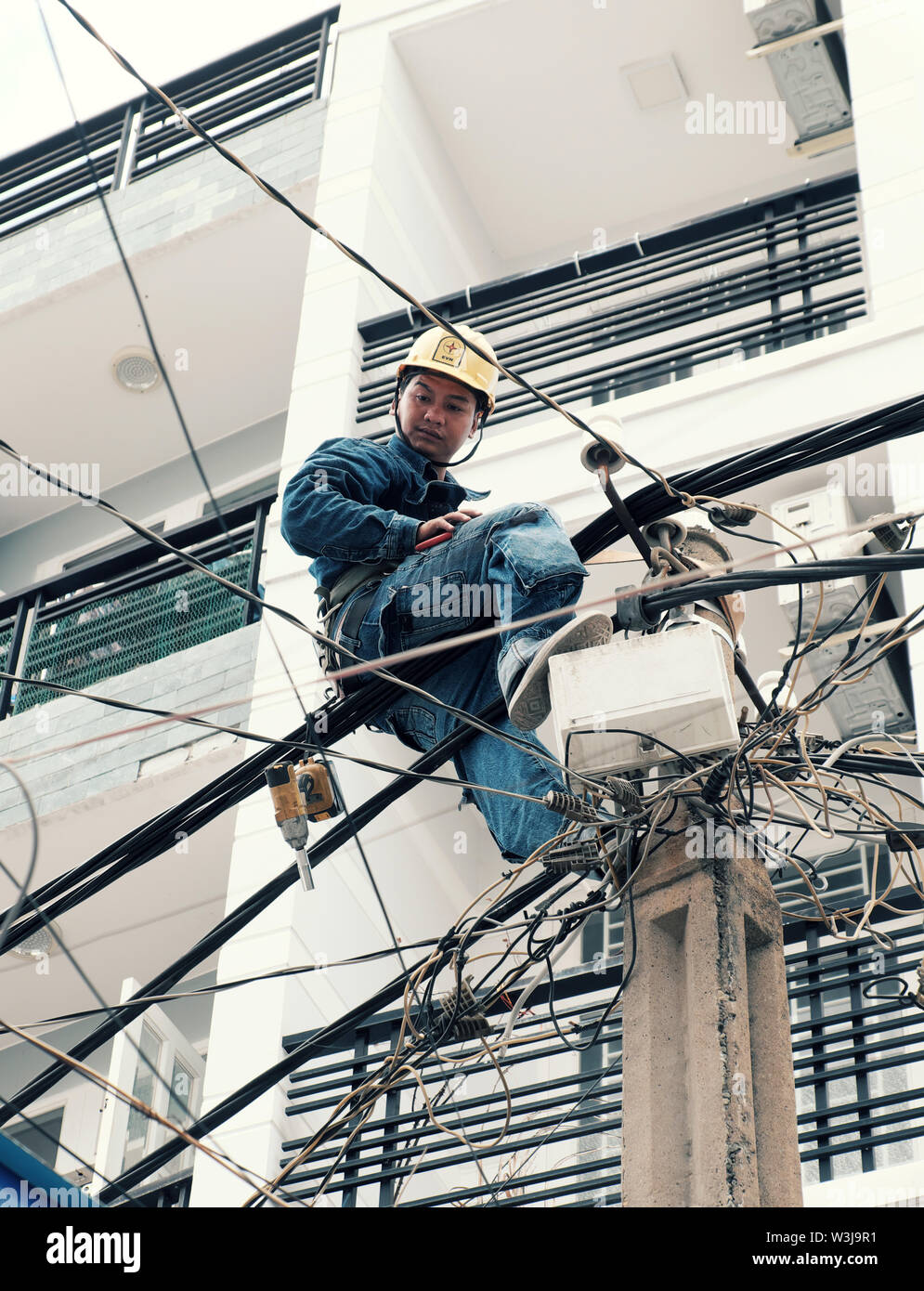 Vietnamesische Strom worker klettern hoch auf elektrische post Strom Netzwerk, Mann Arbeit in unsicheren Service am Mittag, Vietnam, Ho Chi Minh City Stockfoto