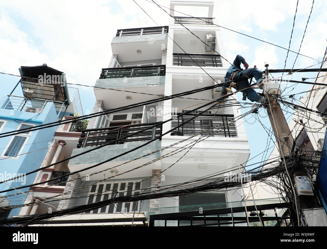 Vietnamesische Strom worker klettern hoch auf elektrische post Strom Netzwerk, Mann Arbeit in unsicheren Service am Mittag zu reparieren, Ho Chi Minh City, Vietnam Stockfoto