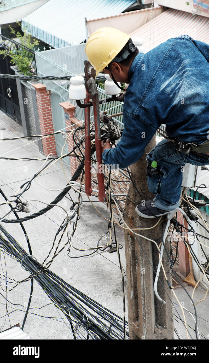 Vietnamesische Strom worker klettern hoch auf elektrische post Strom Netzwerk, Mann Arbeit in unsicheren Service am Mittag zu reparieren, Ho Chi Minh City, Vietnam Stockfoto